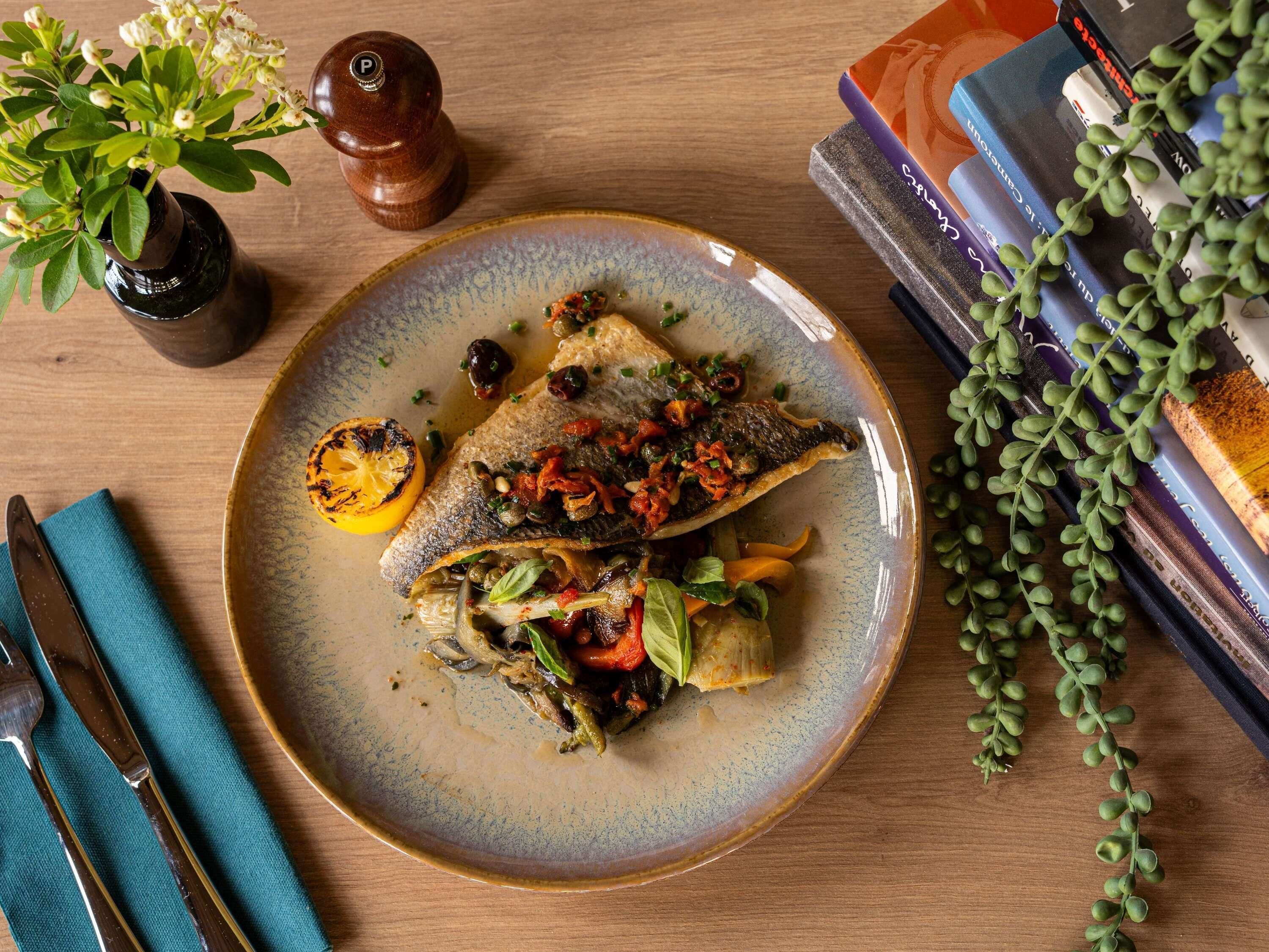 Un plato de comida con pescado, verduras y una rodaja de limón sobre una mesa.
