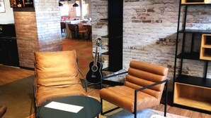 En avslappningshörna med läderfåtöljer, ett runt bord, en gitarr och en tegelvägg.