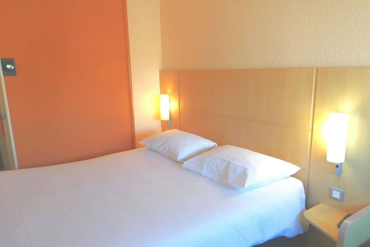 Une chambre d’hôtel avec un lit simple, deux lampes de chevet et une petite table.