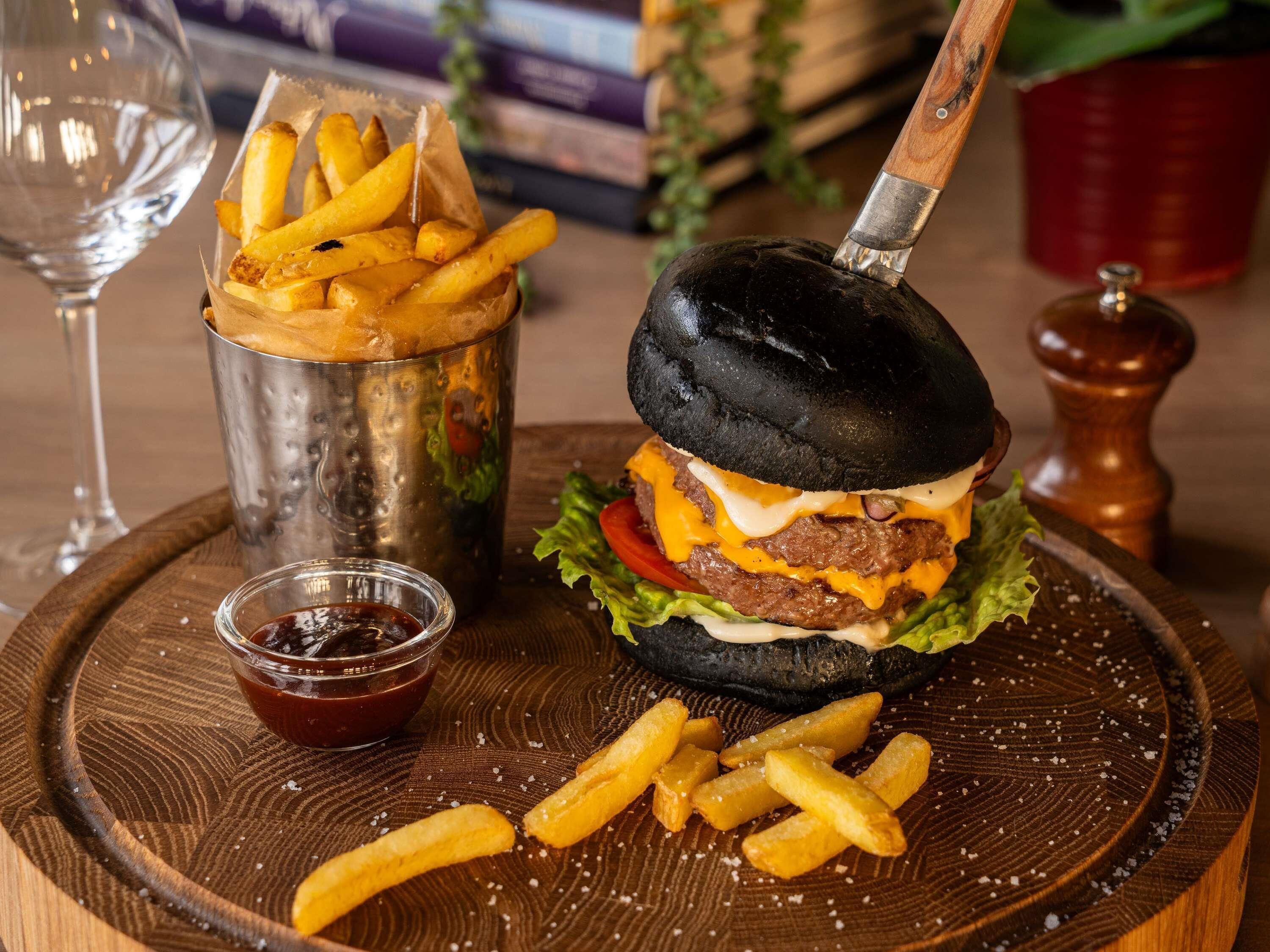 A burger with a black bun, cheese, lettuce, and a beef patty, served with fries and ketchup.