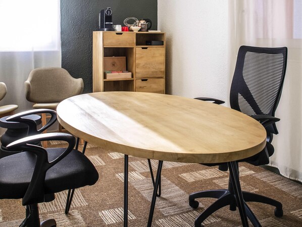 A conference room with a round wooden table, black office chairs, a bookshelf, and a patterned carpet.
