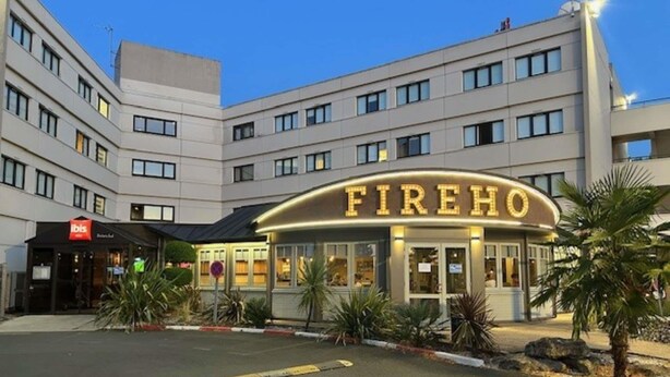 Ett hotell som heter FIREHO, med en modern fasad, flera våningar och en parkeringsplats framför.