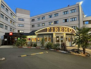 A hotel named FIREHO with a modern facade, multiple floors, and a parking area in front.
