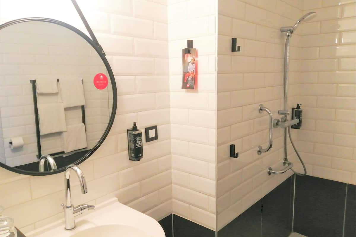 A bathroom with a sink, mirror, towel rack, shower, and toiletries.