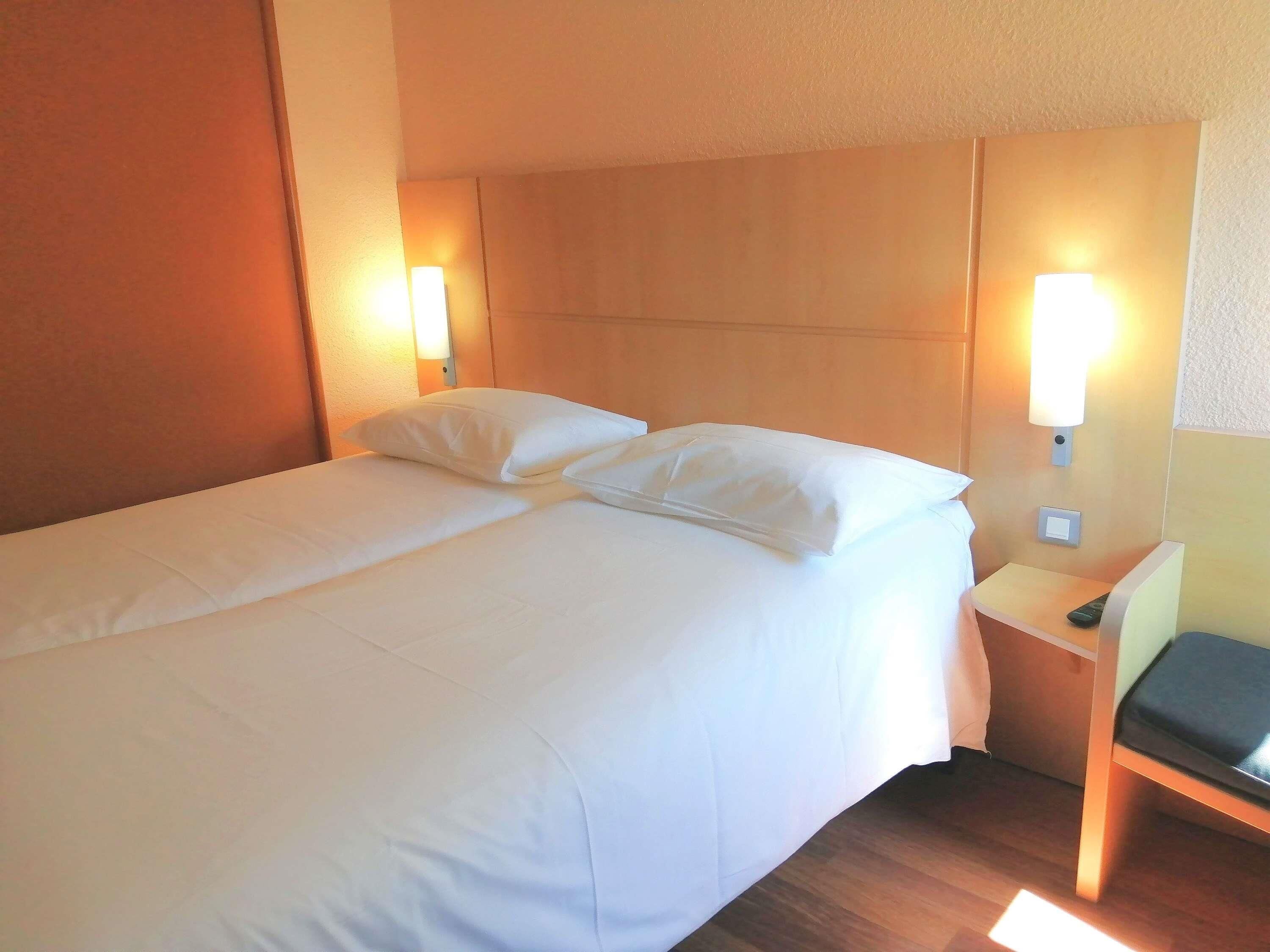 A hotel room with a bed, two bedside lamps, a nightstand, and a chair.
