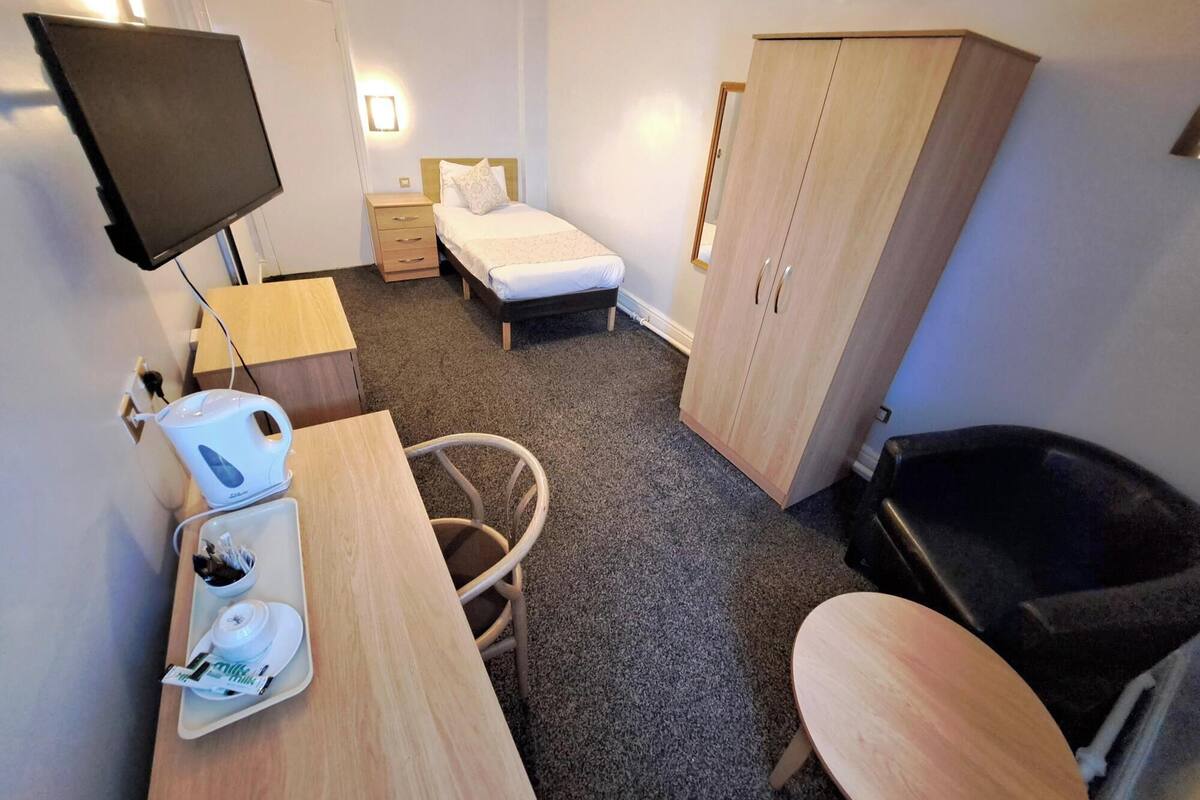 A hotel room with a bed, a desk with a kettle, a TV, a wardrobe, and a bathtub.