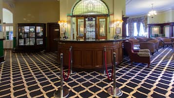 A lobby with a checkered floor, a reception desk, a stained glass window, and a seating area with armchairs.