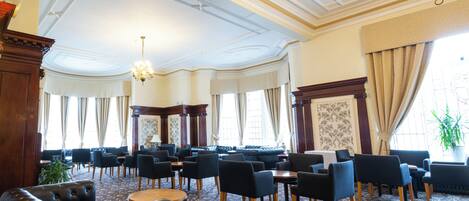 A spacious hotel lobby with a high ceiling, chandeliers, and a patterned carpet.