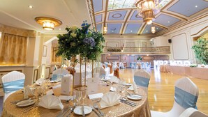 A banquet hall with round tables set for a formal event, featuring gold tablecloths, white napkins, and floral centerpieces.