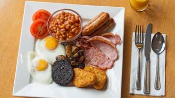 A plate of breakfast food including eggs, bacon, sausages, beans, tomatoes, and toast.