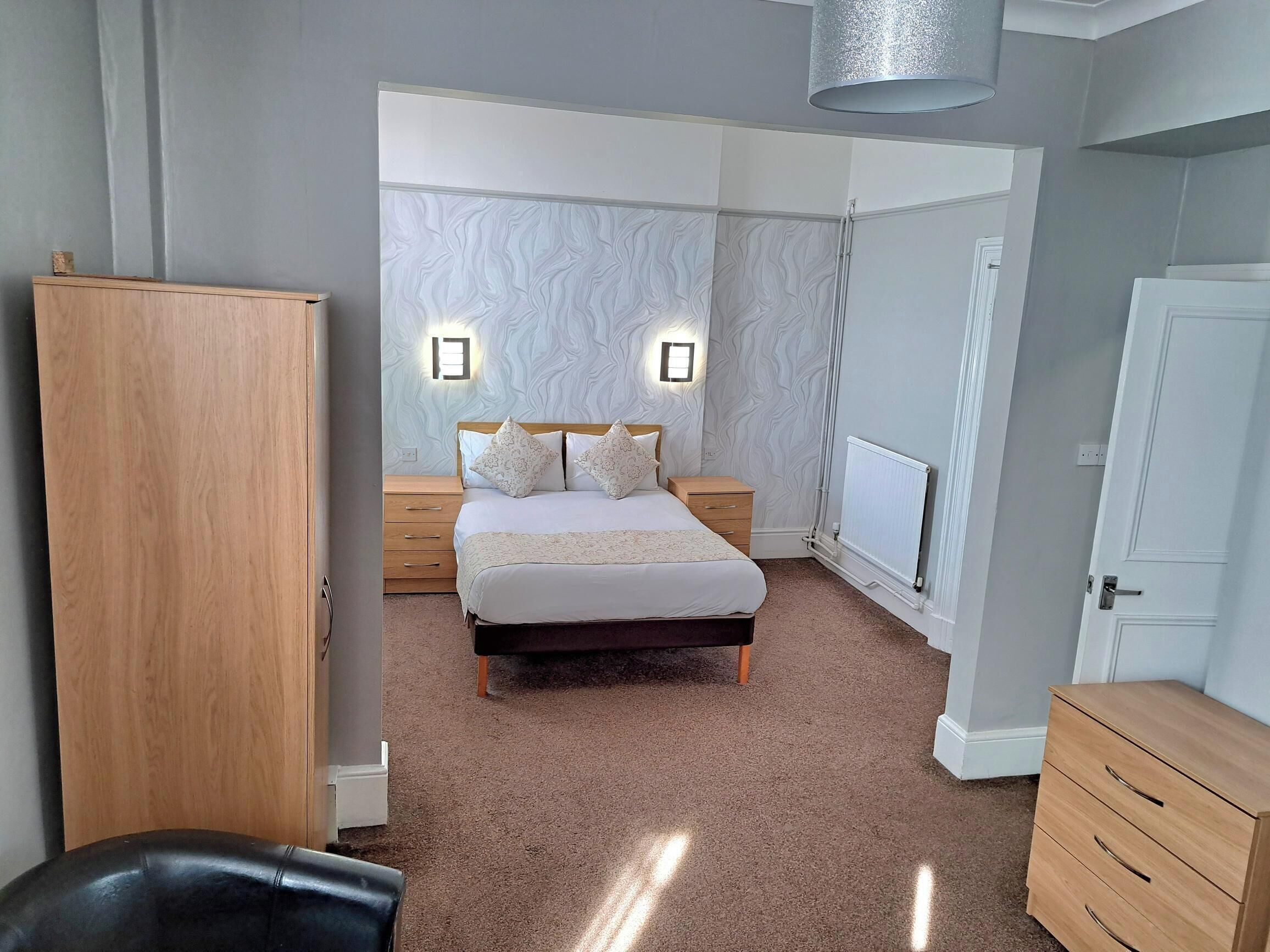 A bedroom with a bed, bedside tables, a wardrobe, and a radiator.