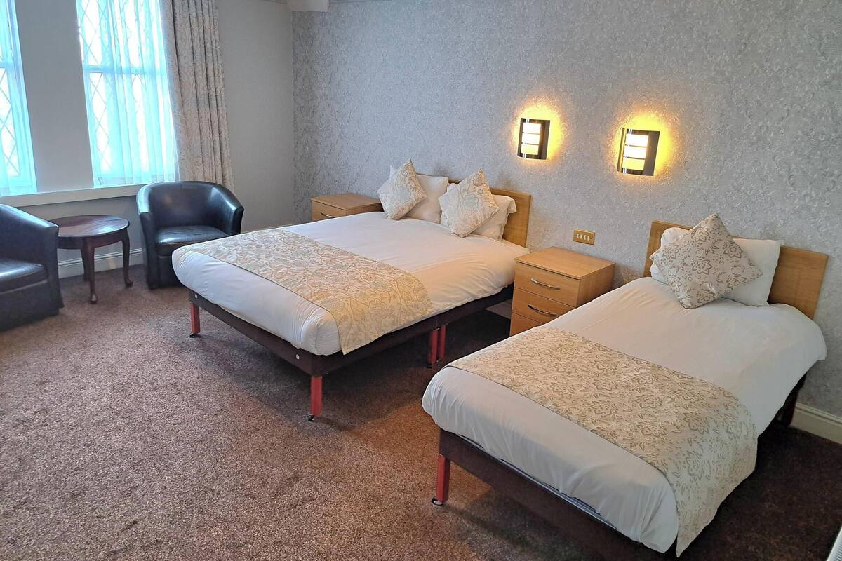 A hotel room with two beds, a chair, a small table, and a lamp.
