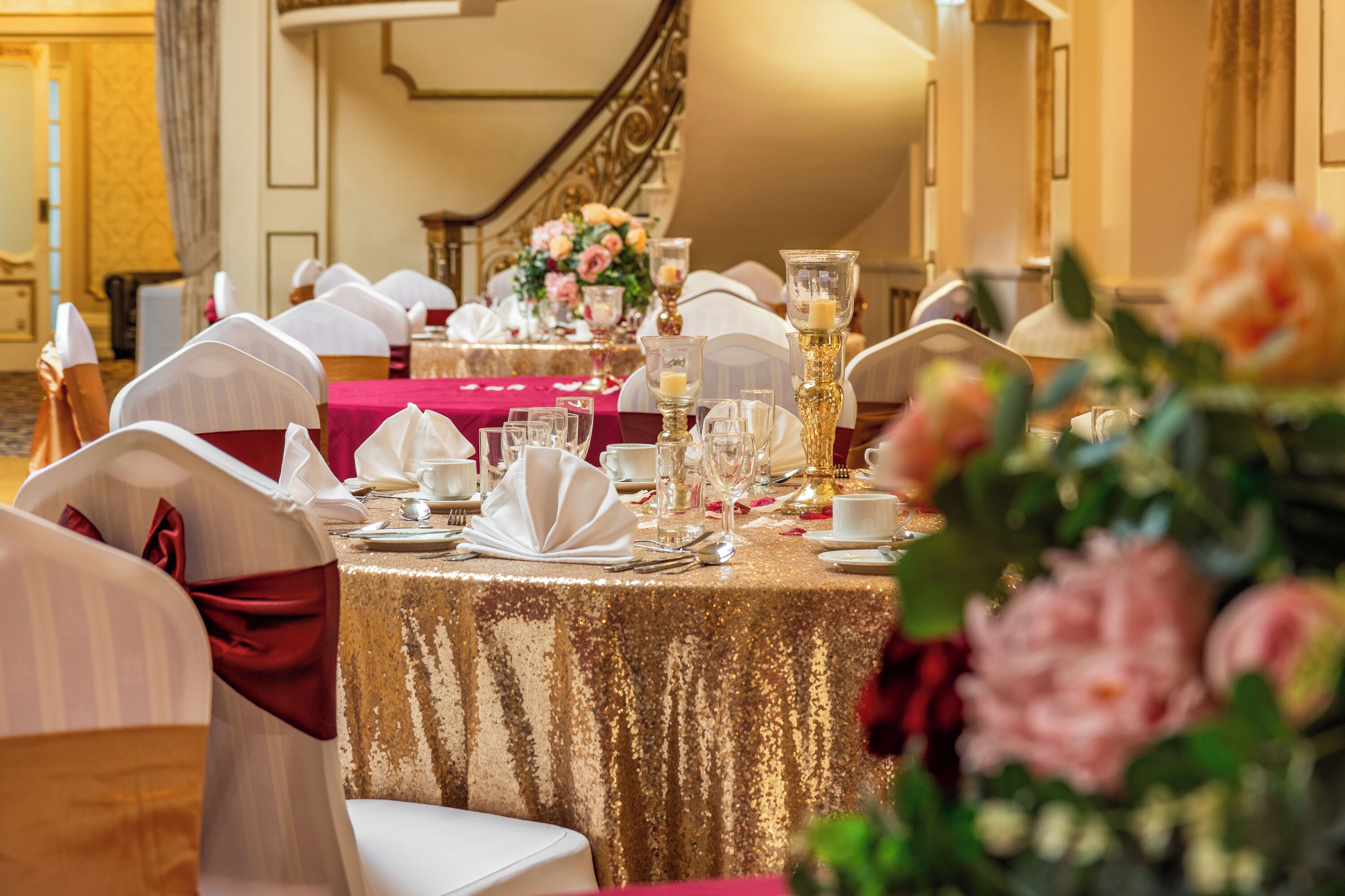A banquet table set with white tablecloths, gold accents, and floral centerpieces.