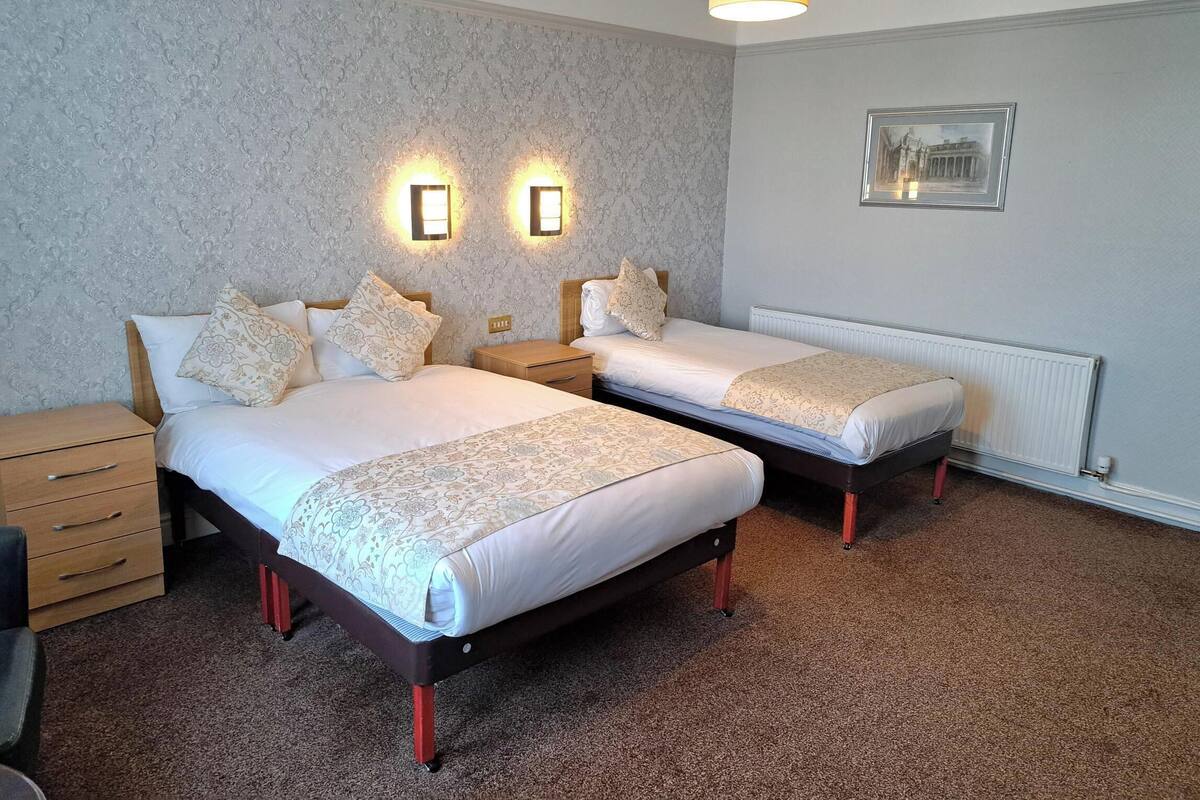 A hotel room with two beds, a wooden nightstand, a small table, and a framed picture on the wall.