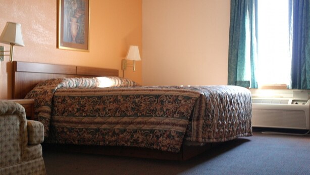A hotel room with a bed, a chair, a painting on the wall, and a window with curtains. - State Line Inn (Hagerstown)