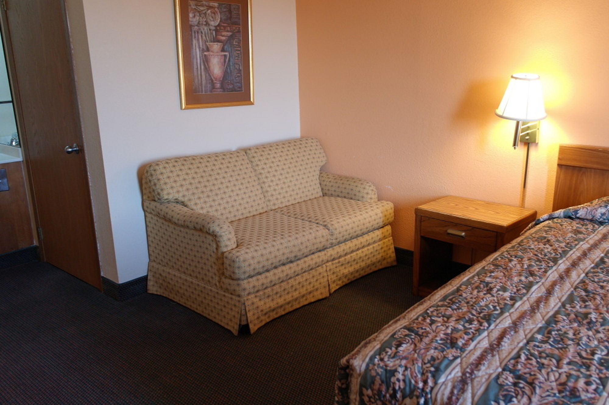 Habitación de hotel con sofá, mesita de noche, lámpara y cama con colcha estampada.