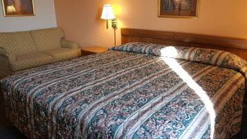 A hotel room with a large bed, a sofa, a nightstand, and a lamp.