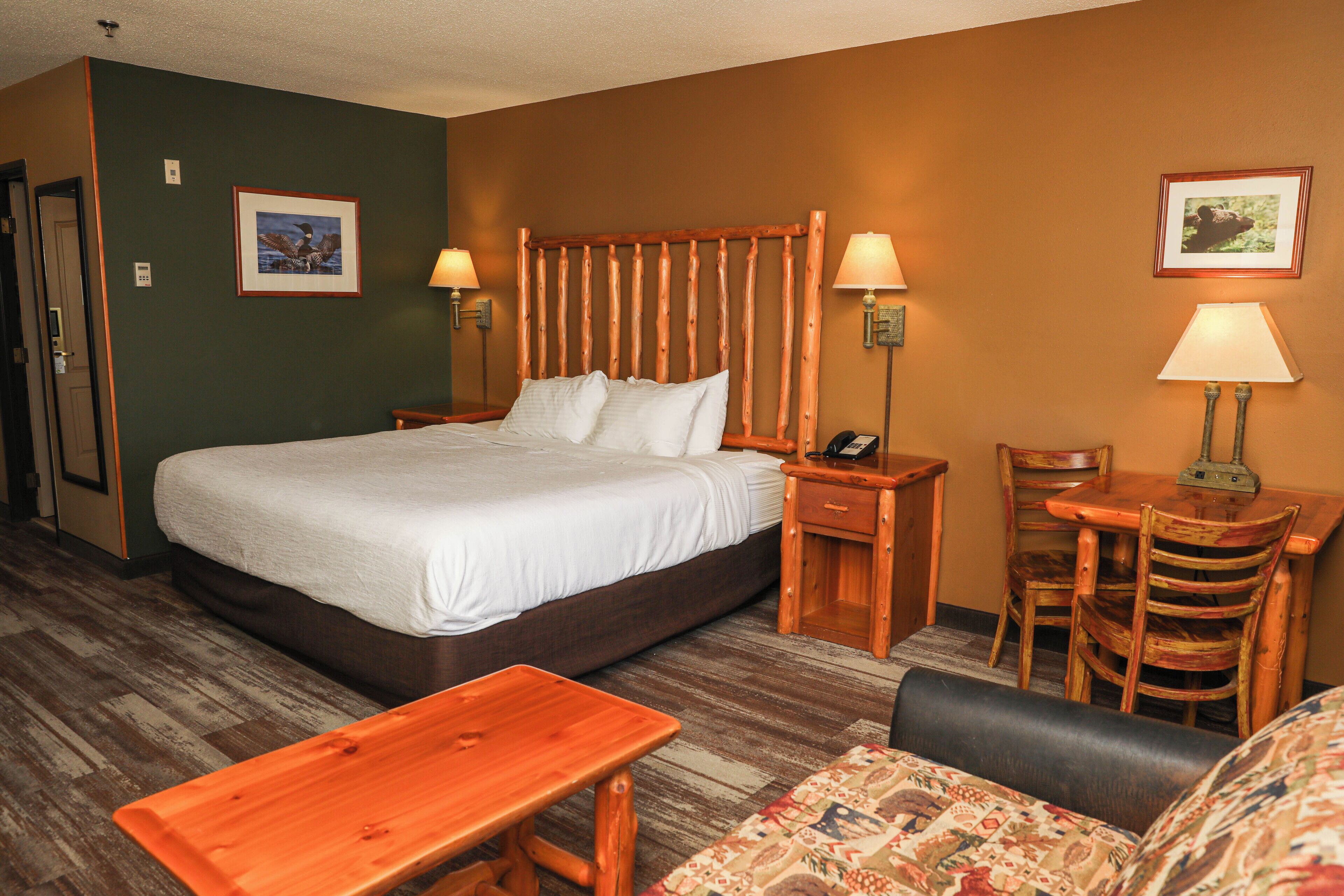 A hotel room with a large bed, two bedside tables with lamps, a wooden desk with a chair, and a small sofa.