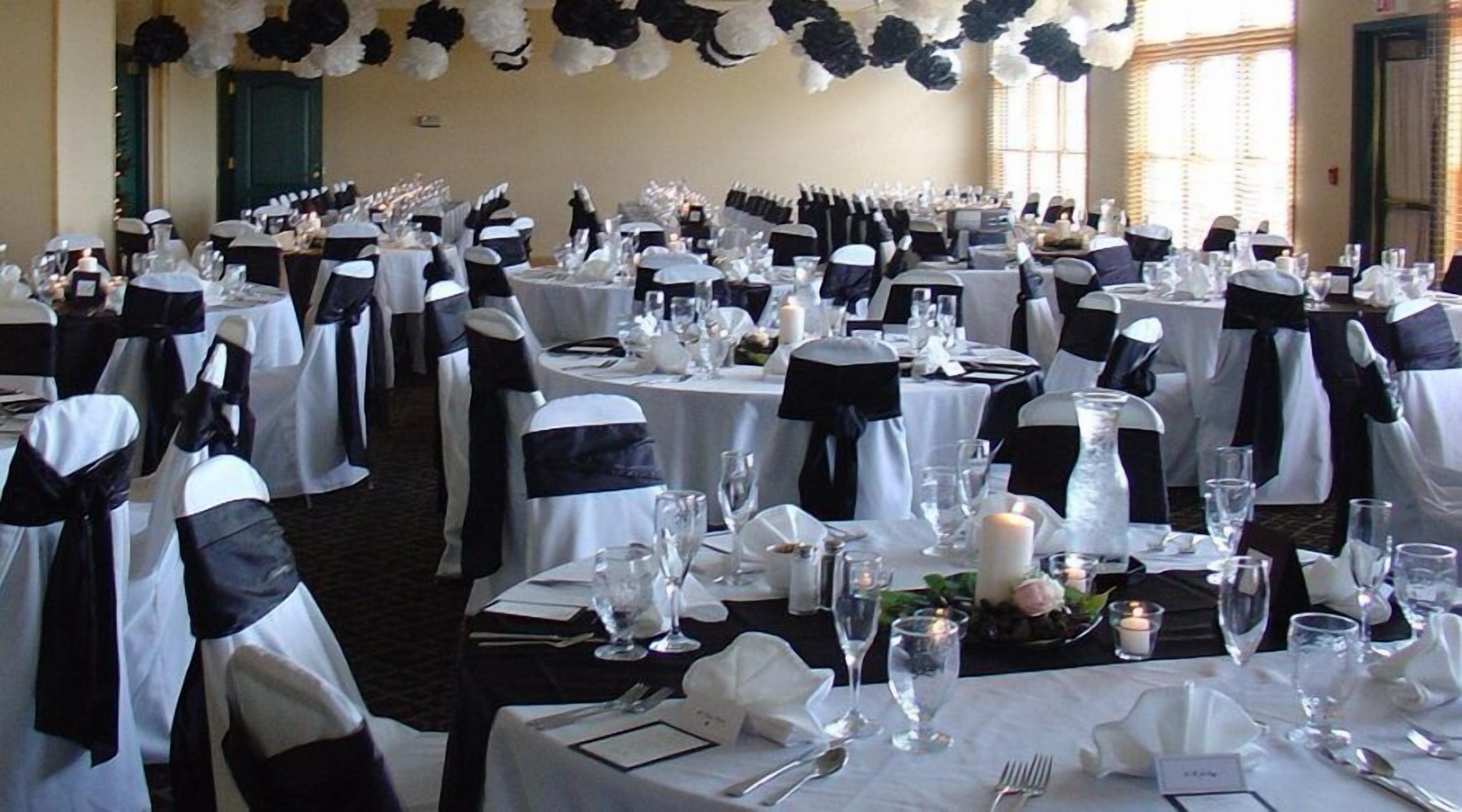 A banquet hall with round tables set for a formal event, each with white tablecloths, black sashes, and candles.