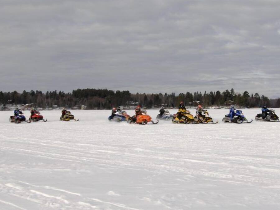 Un grupo de motos de nieve en un campo nevado, con un bosque al fondo.