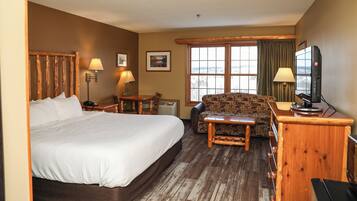 A hotel room with a large bed, a sofa, a desk with a computer, and a window with curtains.