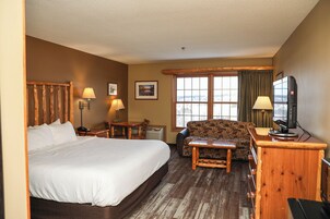 A hotel room with a large bed, a sofa, a desk with a computer, and a window with curtains.