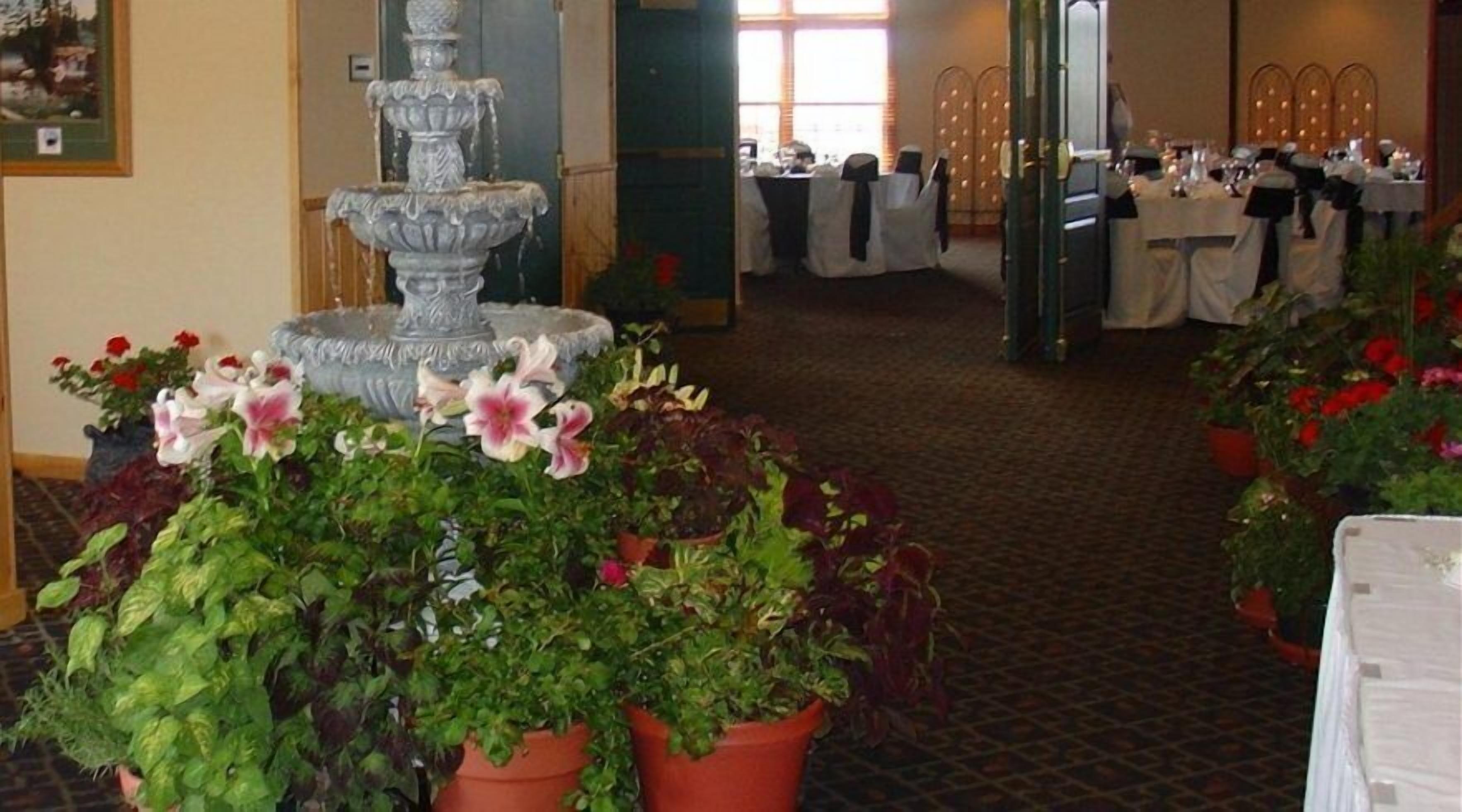 A hotel lobby with a fountain, potted plants, and tables set up for a reception area.