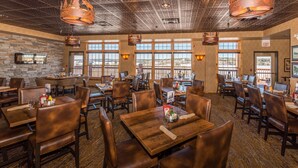 A restaurant interior with multiple dining tables and booths, large windows, and hanging copper chandeliers. - Grand Ely Lodge Resort & Conference Center (Ely)