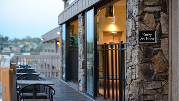 An outdoor seating area with tables and chairs, a stone wall with an 'Entry 3rd Floor' sign, and a view of the city in the background. - Best Western Plus Landing View Inn & Suites (Branson)