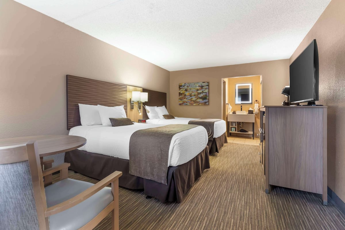 A hotel room with two beds, a desk, a chair, a television, and a bathroom visible through an open door.