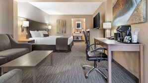A hotel room with a bed, a desk, a chair, a sofa, a TV, and a painting on the wall. - Best Western Plus Landing View Inn & Suites (Branson)
