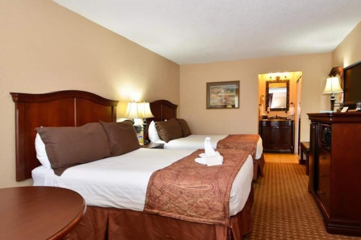 A hotel room with two beds, a desk, a dresser, and a mirror.