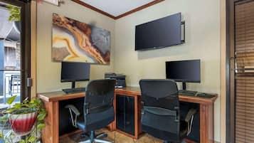 A hotel office with two desks, two monitors, a painting, and an exit sign.