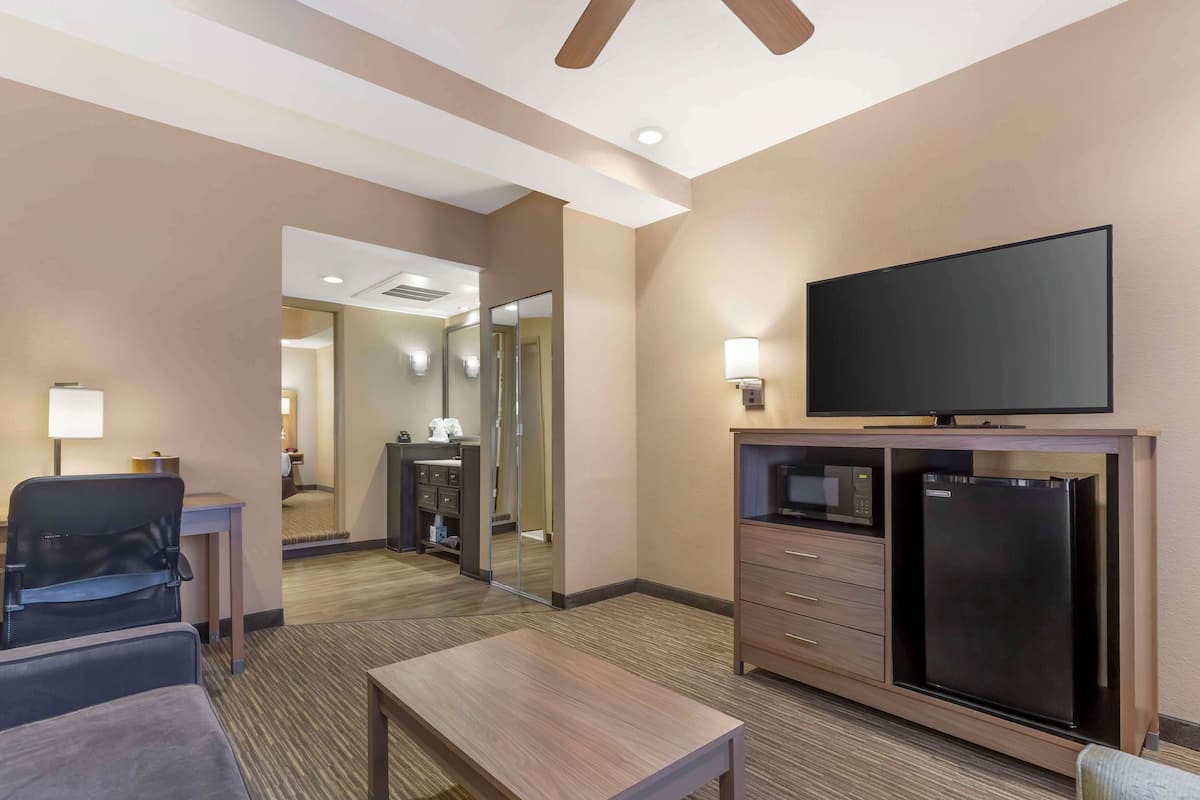 A hotel room with a flat-screen TV, a refrigerator, a microwave, a desk, and a chair.
