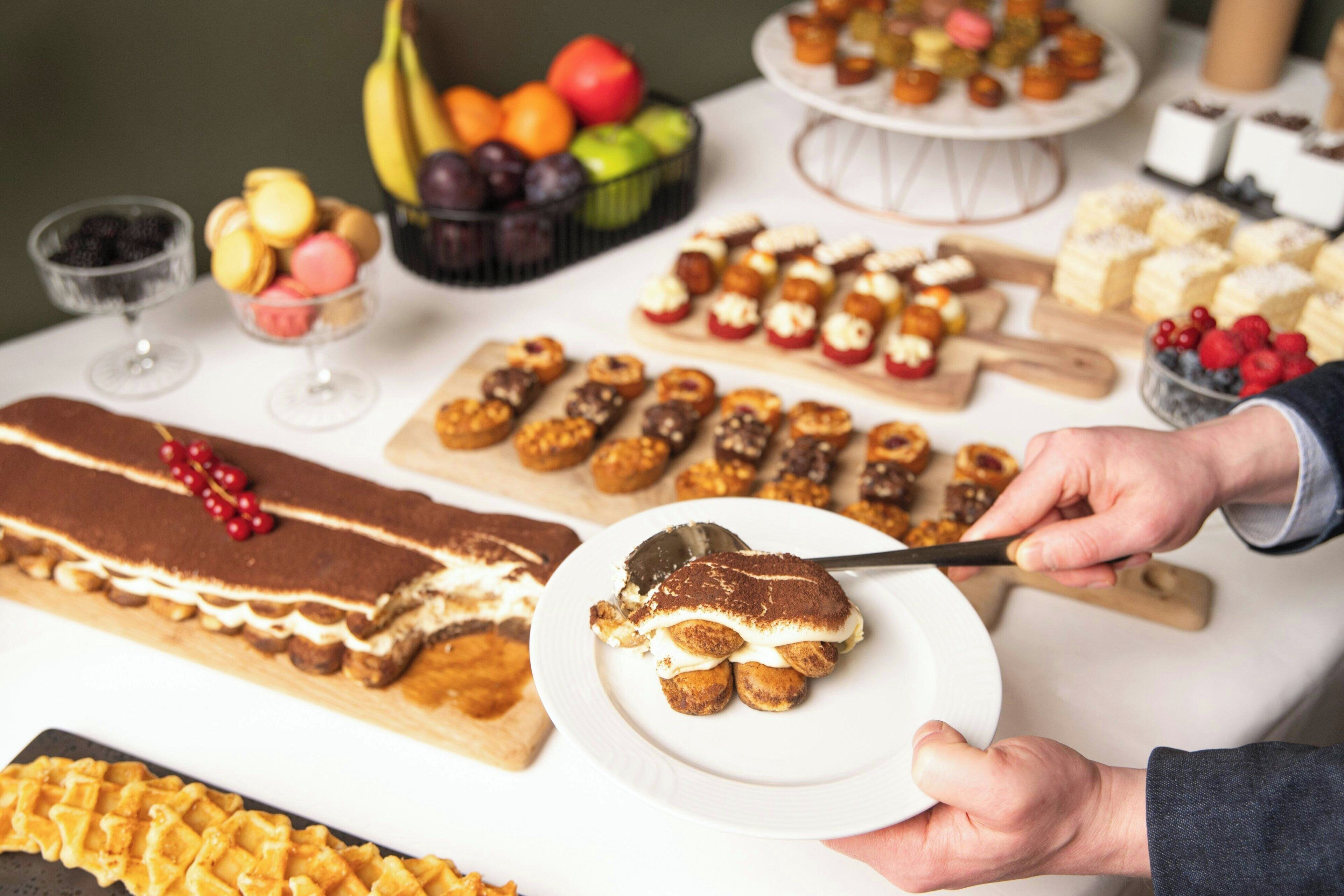 Variedad de postres sobre una mesa, incluyendo un pastel grande de varias capas, macarons y pastelería surtida.