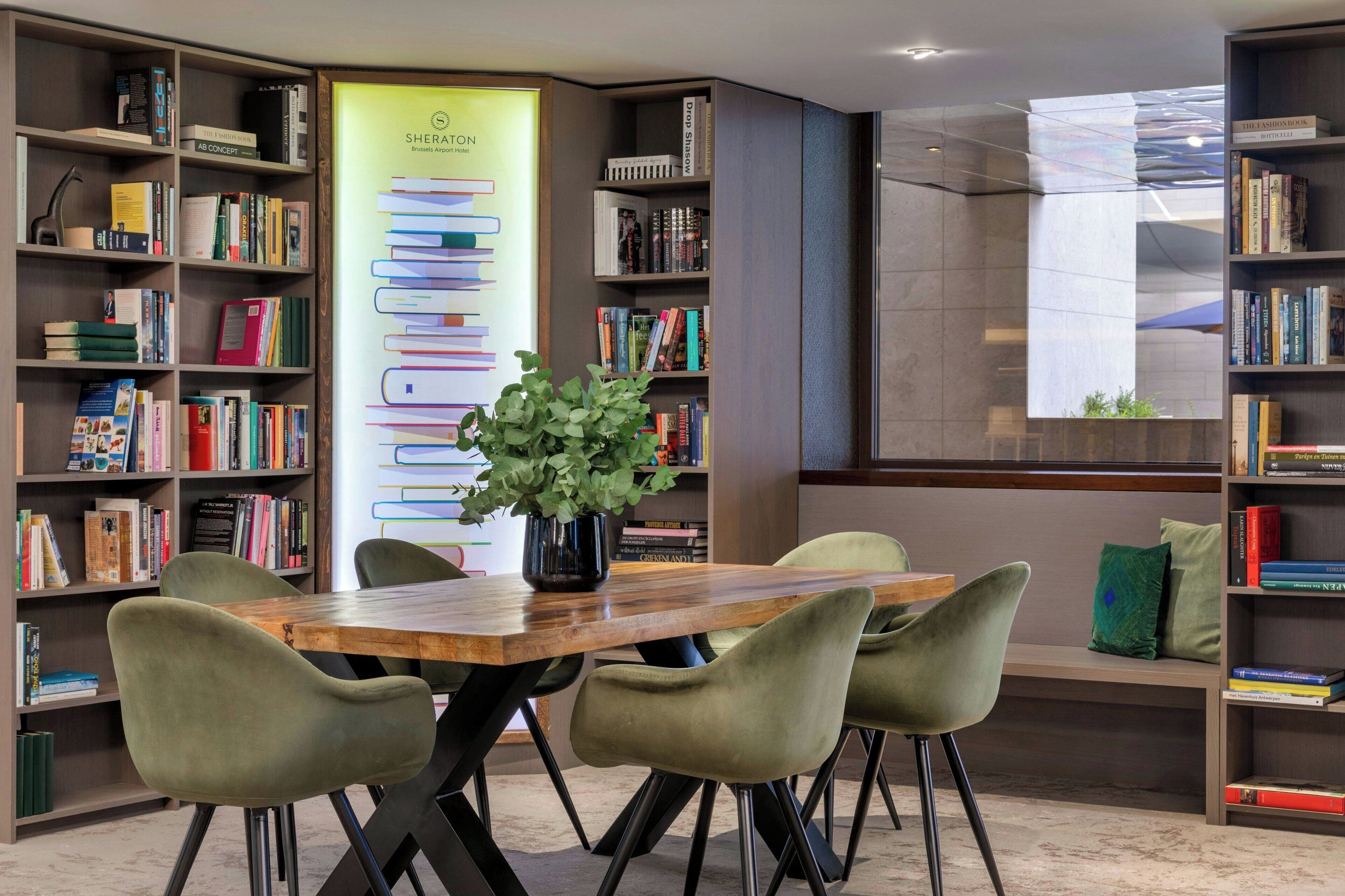 A modern library with bookshelves, a wooden table, and green chairs.