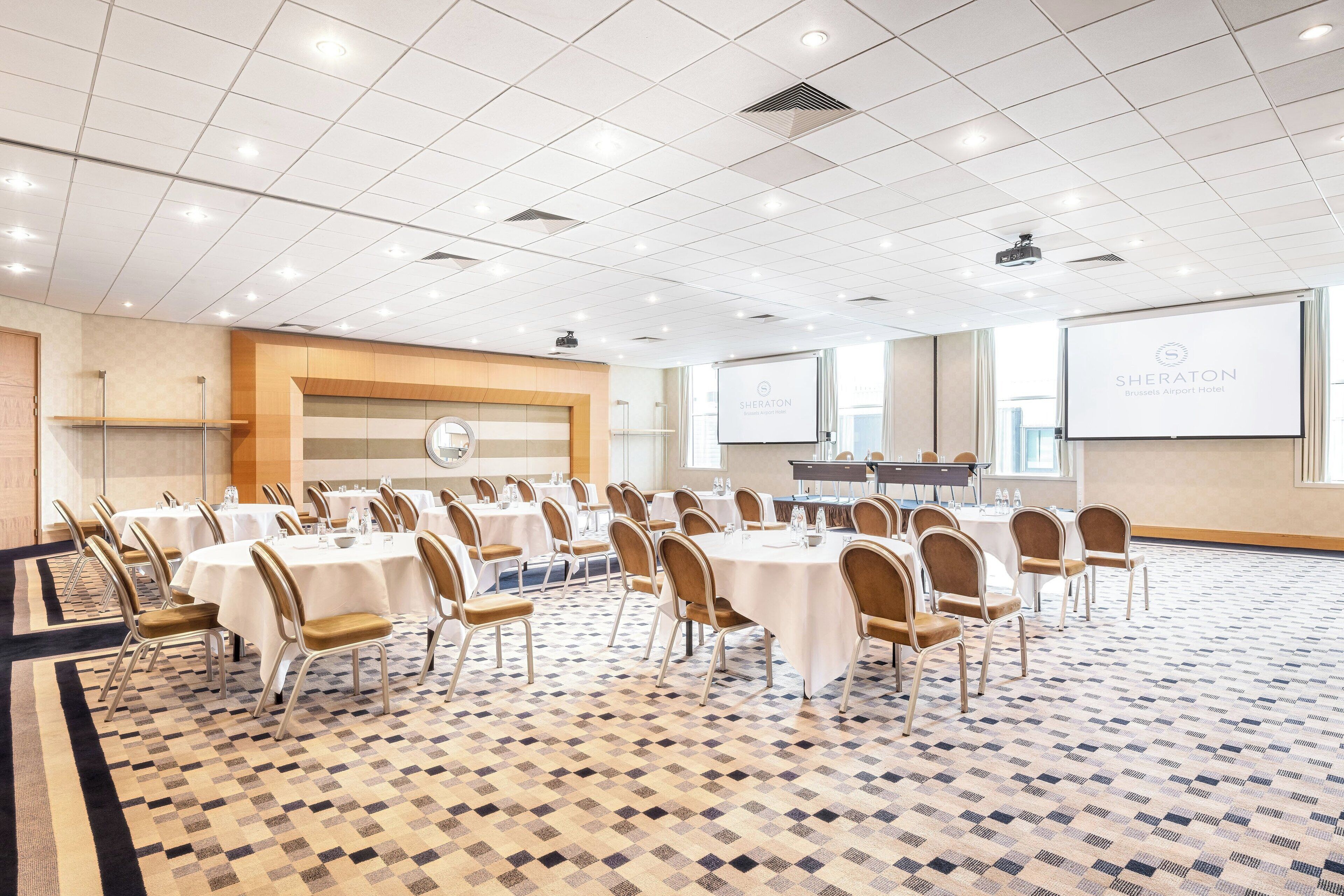 A conference room with round tables and chairs, a projector screen, and a presentation screen.
