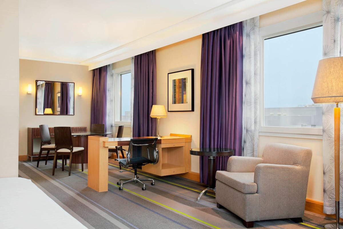 Une chambre d’hôtel comprenant un lit, un bureau avec une chaise, un ordinateur, un canapé et une fenêtre avec des rideaux.