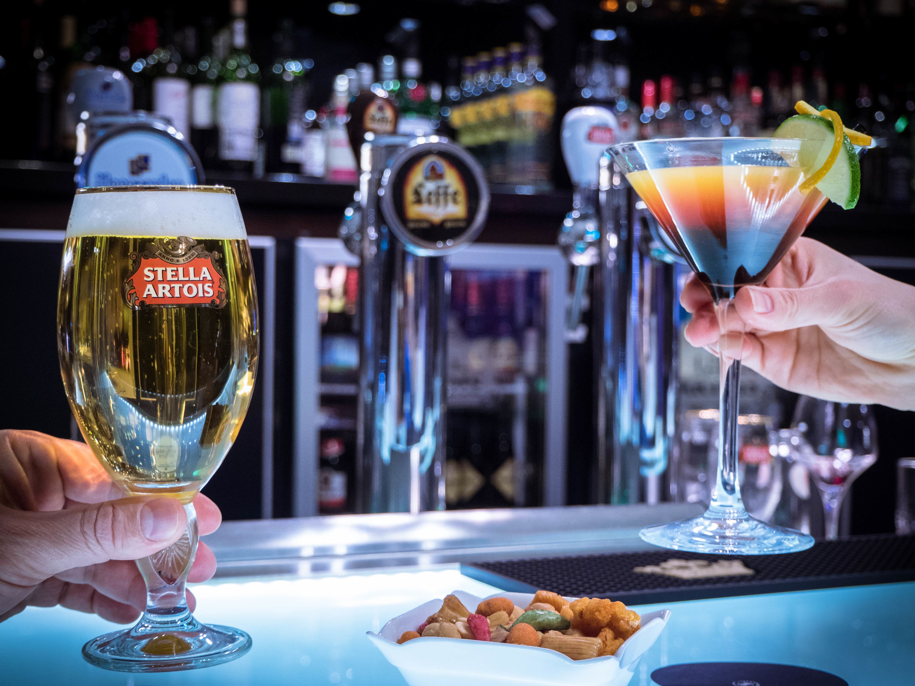 A bar setting with two glasses of beer and a cocktail, a beer tap, and a small bowl of nuts.