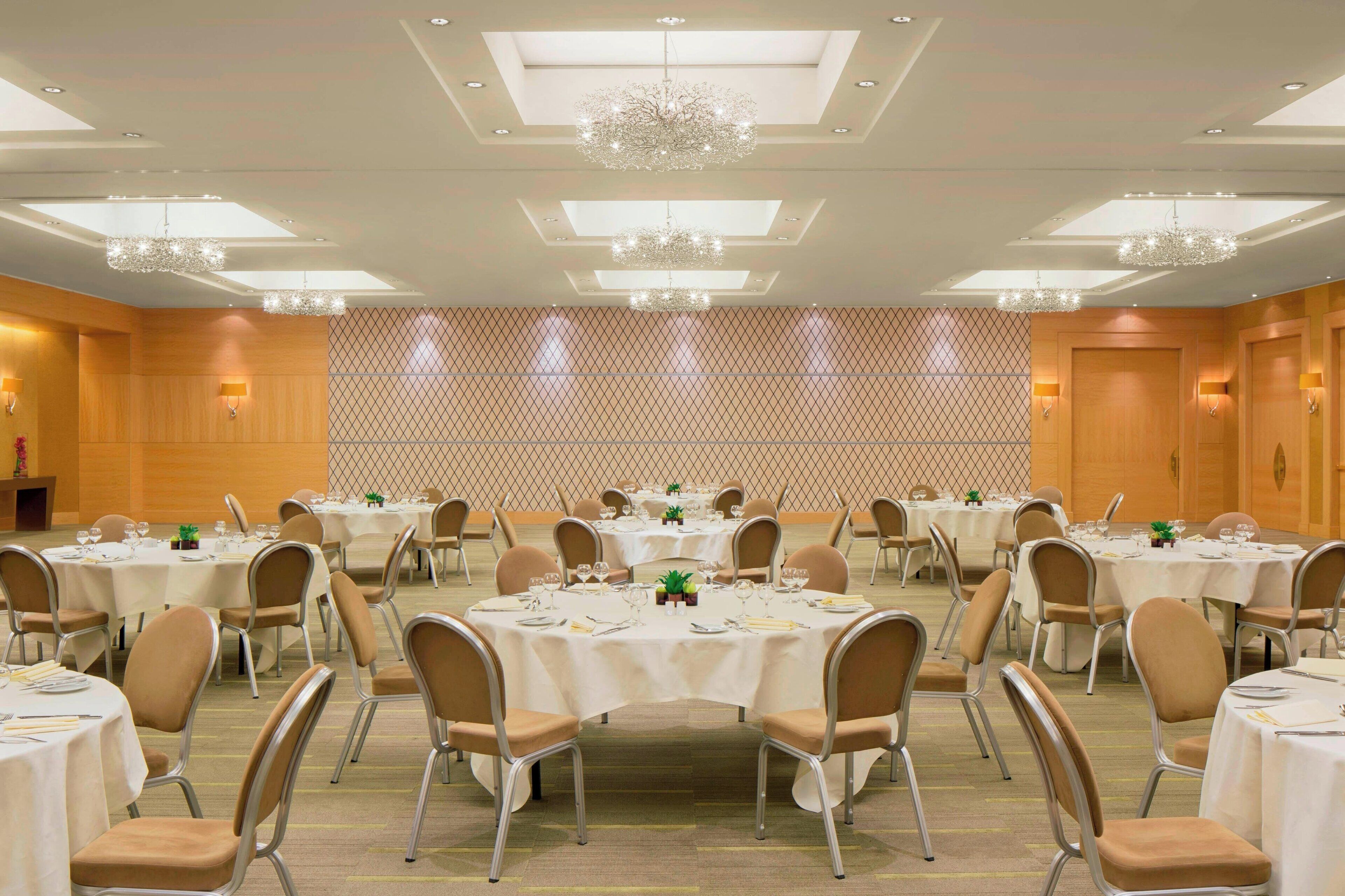 A banquet hall with round tables, chairs, and chandeliers.