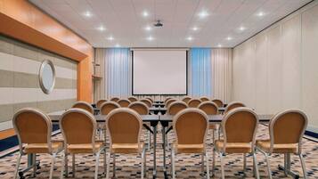 Una sala de conferències amb una taula gran, cadires, una pantalla de projector i una catifa estampada.