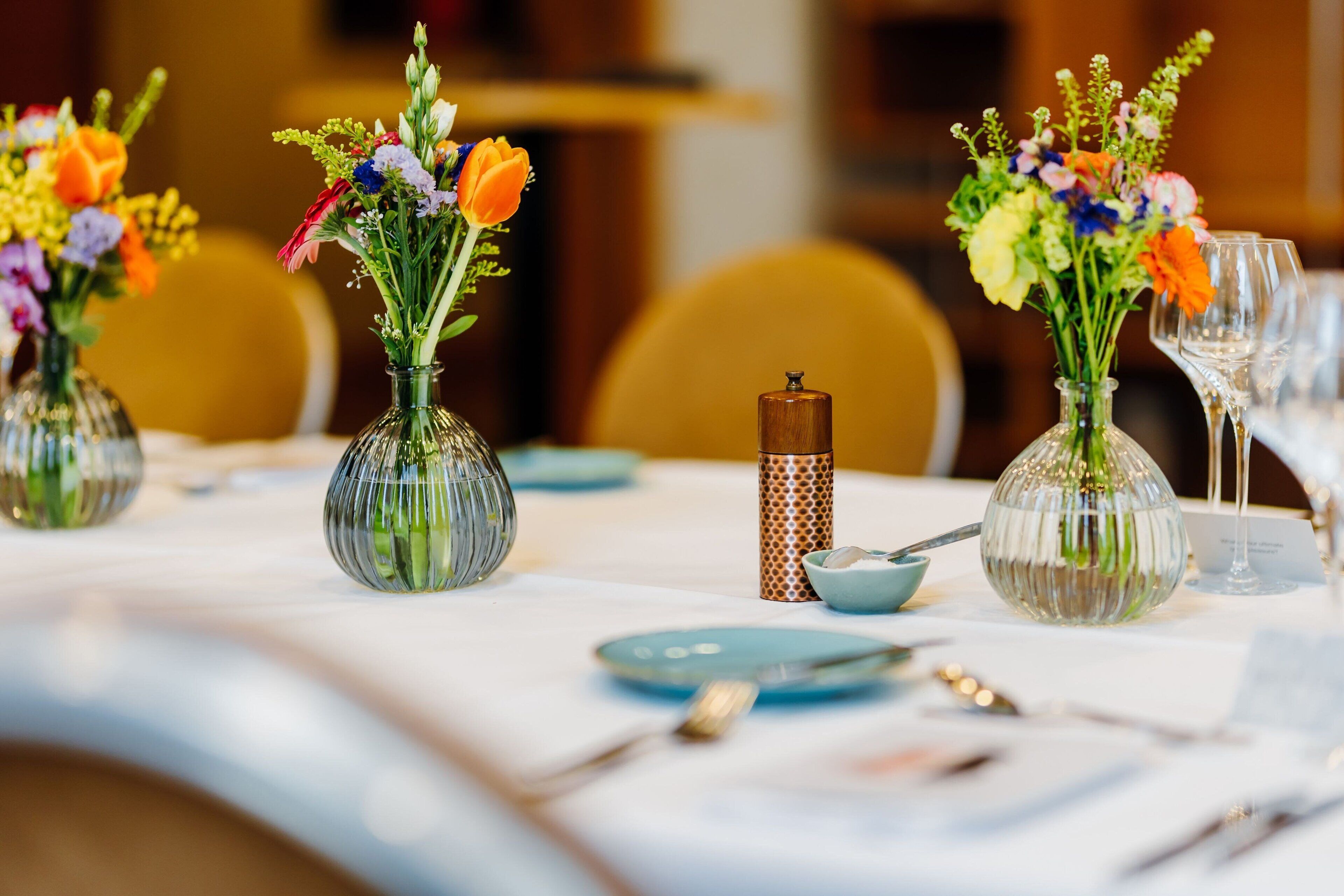 Una mesa dispuesta con jarrones de cristal con flores, platos y cubiertos.