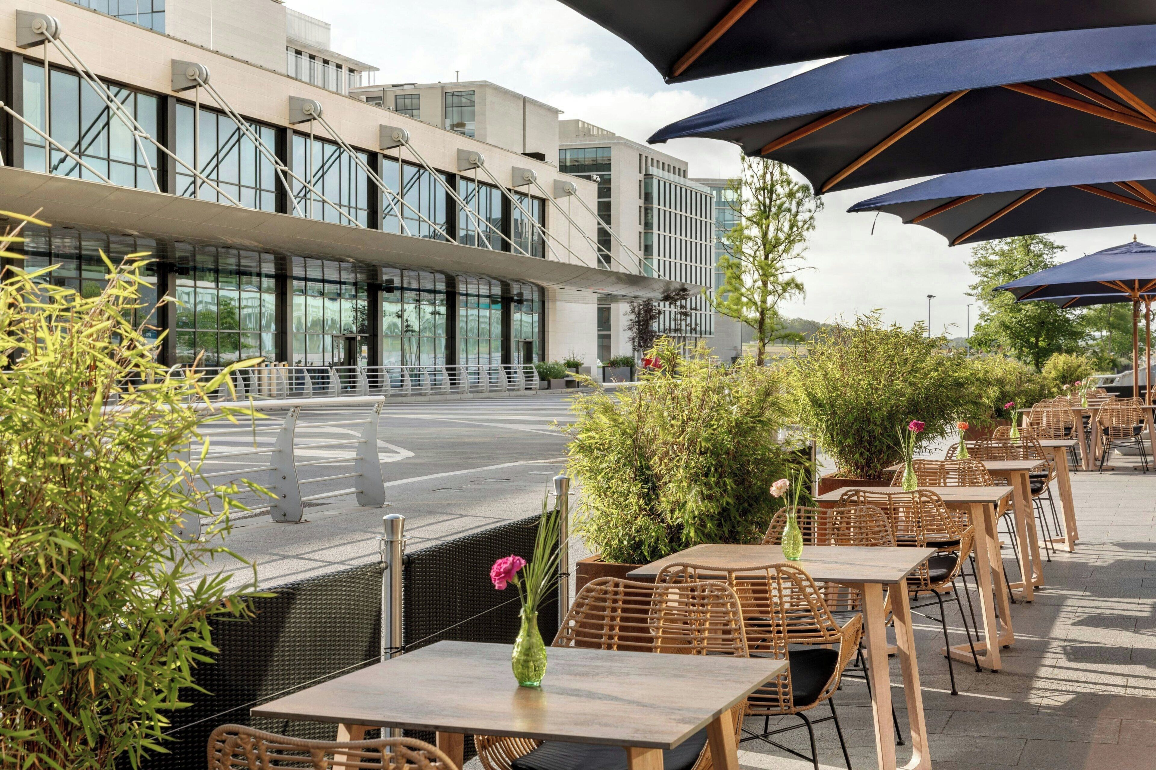 An outdoor seating area with tables and chairs, surrounded by greenery and modern buildings.