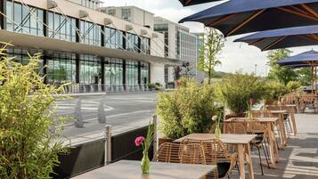 An outdoor seating area with tables and chairs, surrounded by greenery and modern buildings.