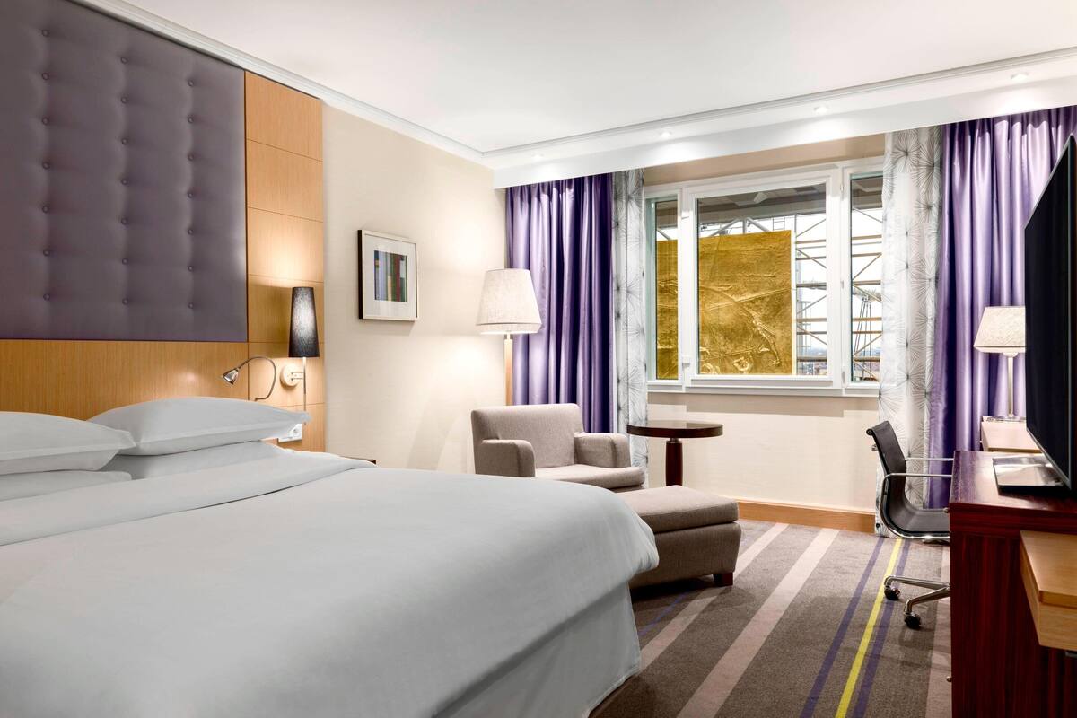 Une chambre d’hôtel avec un grand lit, un bureau, une chaise et une fenêtre avec des rideaux.