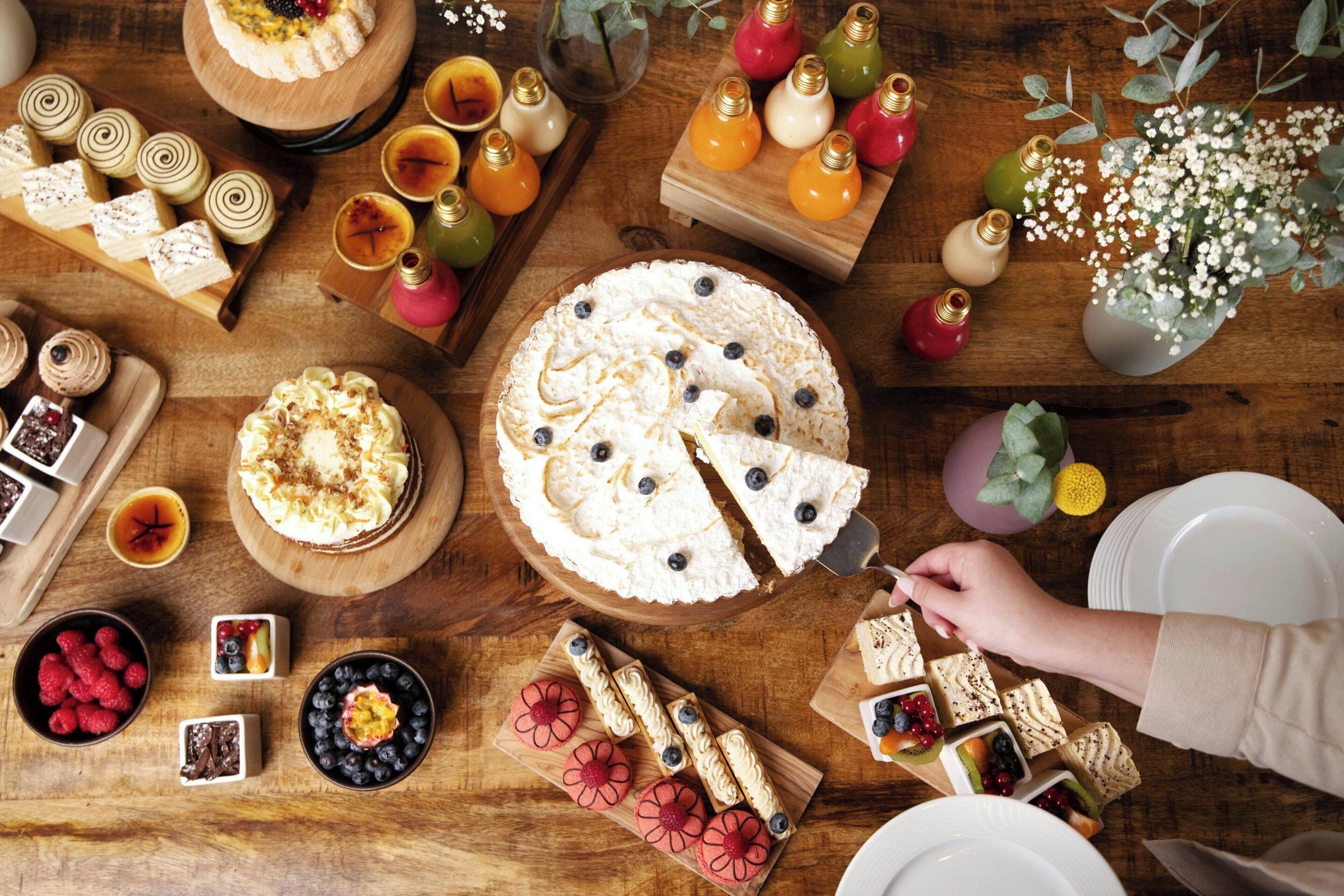Diverse desserts en gebak op een houten tafel, waaronder een taart waarvan een plak wordt geserveerd.