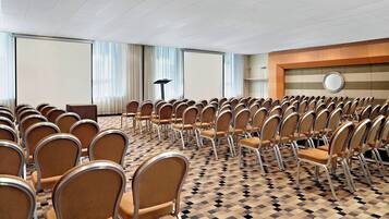 A conference room with rows of chairs, a projector screen, and a large window with curtains.
