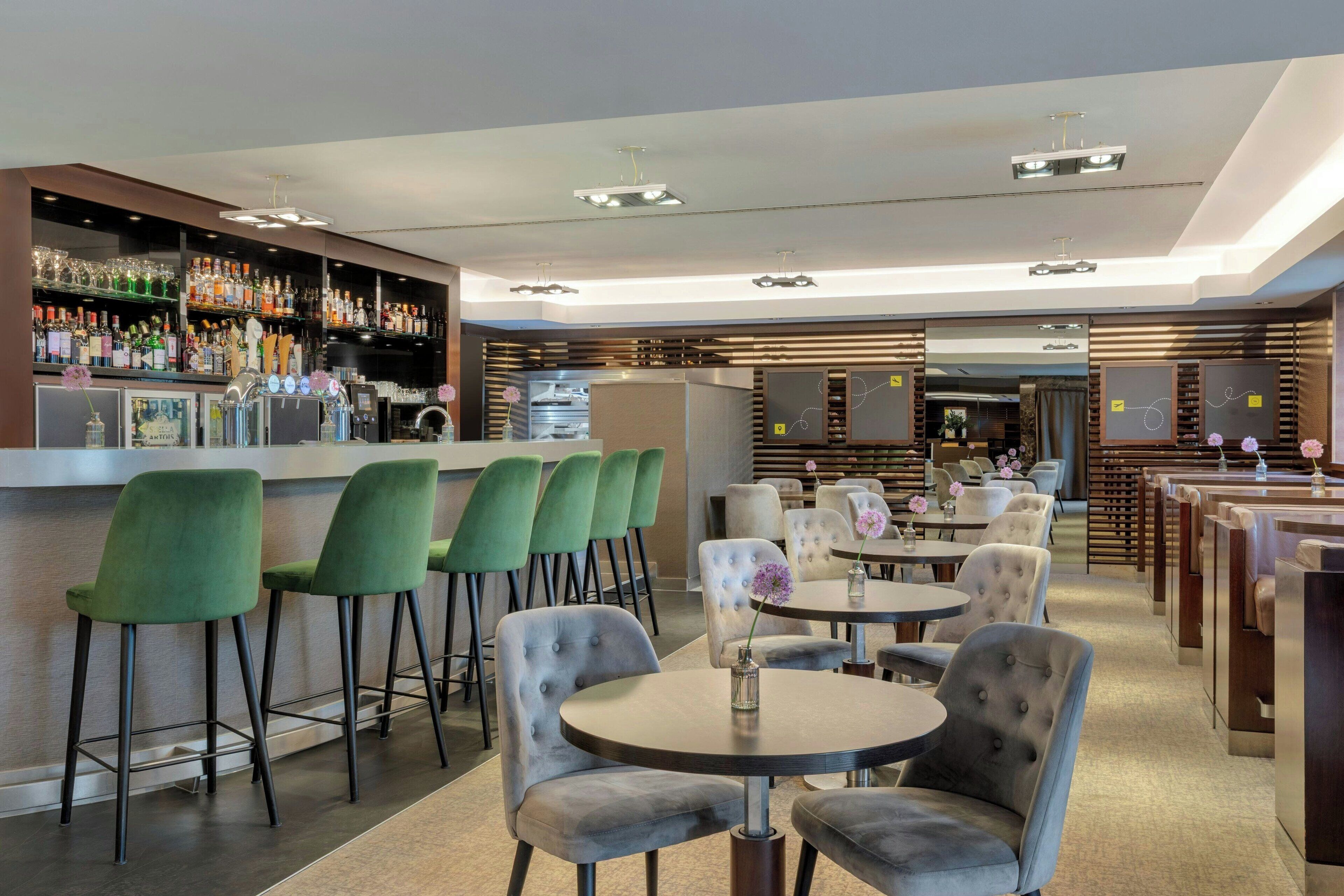 Un espace bar moderne offrant différents types de sièges, notamment des tabourets de bar et des tables rondes, ainsi qu'un comptoir de bar bien garni.
