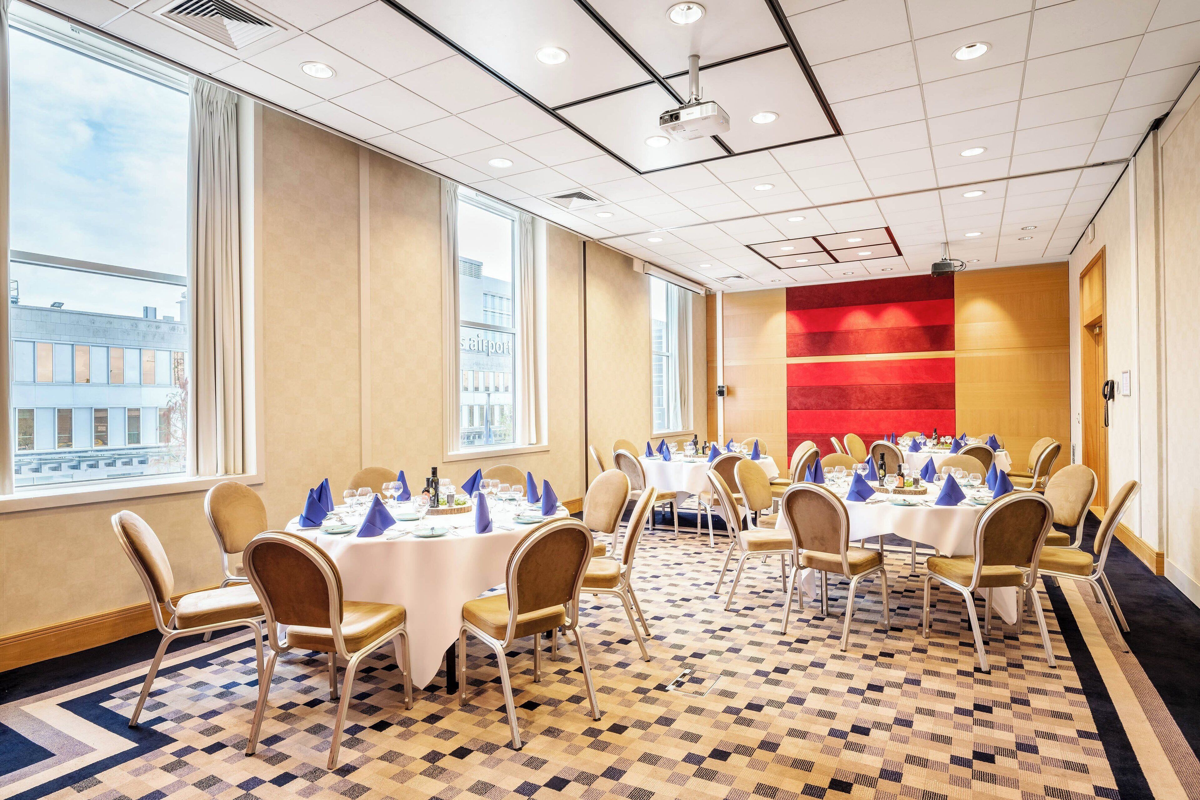 A conference room with multiple tables and chairs, large windows, and a patterned carpet.