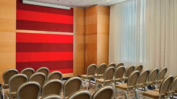 A conference room with rows of beige chairs, a red and beige wall, and a large window with sheer curtains.